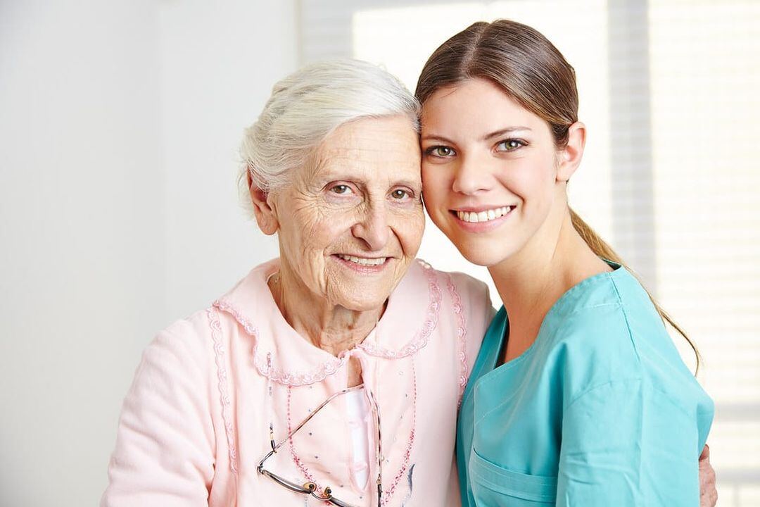 Caregiver in scrubs embracing a happy senior woman